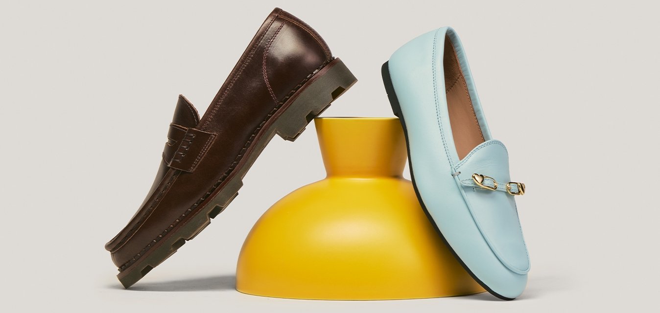 Hnědý kožený mokasín a světle modrý kožený mokasín opřený o žlutou keramickou vázu na neutrálním pozadí.
