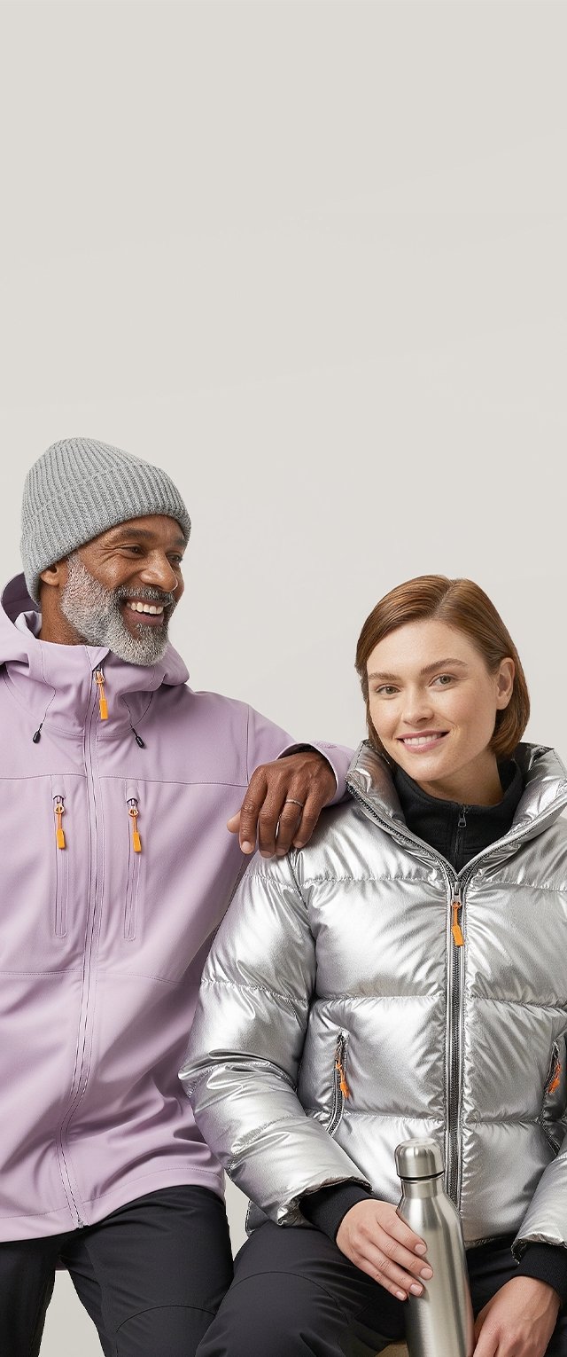 Uomo sorridente con giacca lavanda e berretto grigio, con la mano sulla spalla di una donna in giacca argentata, che tiene una bottiglia in acciaio inossidabile.