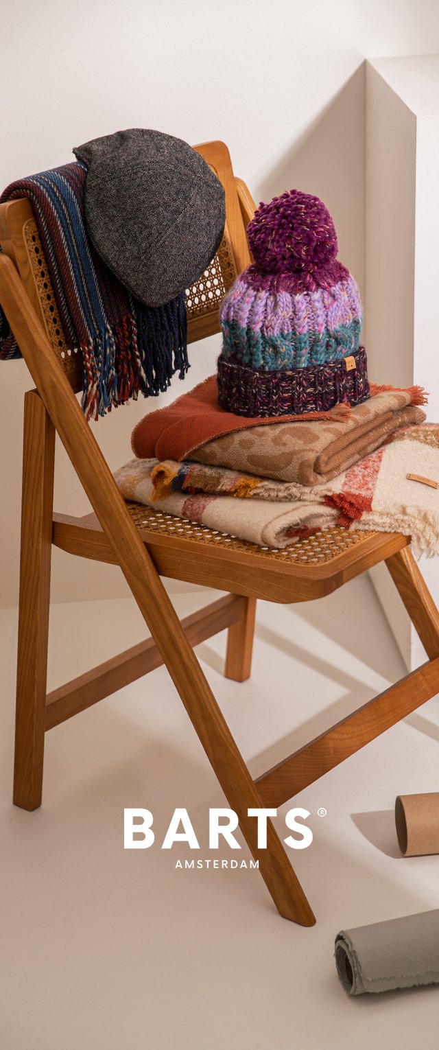 Wooden folding chair with a woven seat. A black beanie and a purple pom-pom hat atop rolled scarves in various textures and colors.