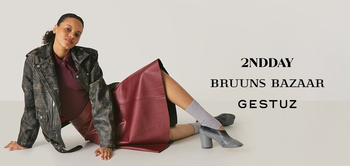 Žena ležící na podlaze, oblečená v bordové kožené sukni, vzorované černé bundě, šedých ponožkách a stříbrných botách na blokovém podpatku.