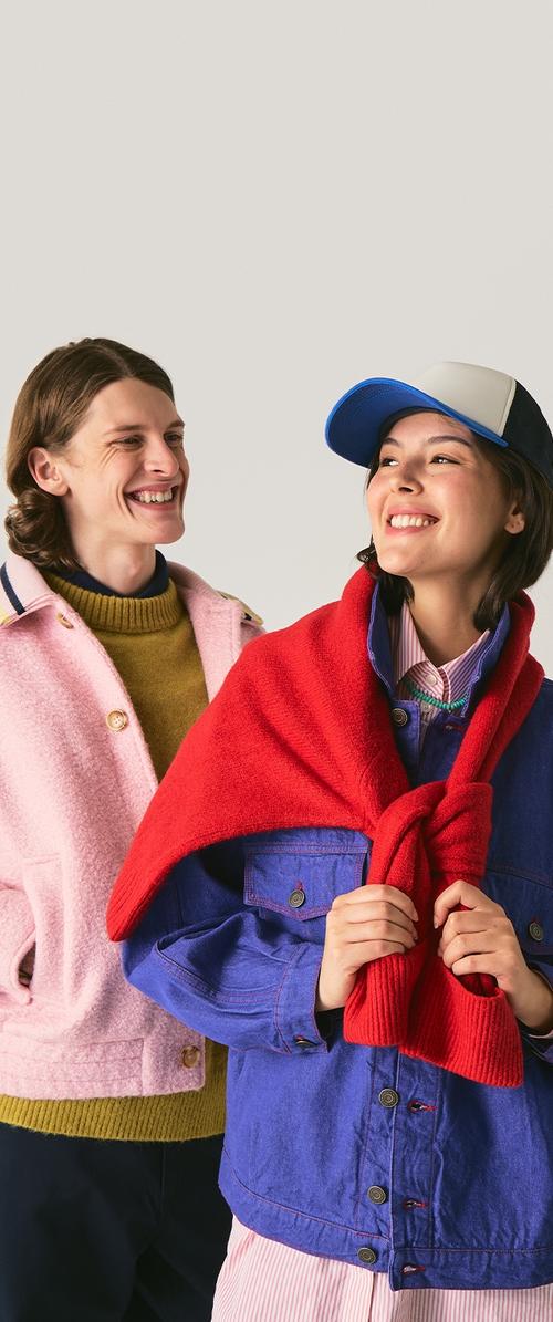 Due individui indossano abbigliamento esterno colorato: un giubbotto fluffy rosa, un pullover di maglia verde e un giubbotto di jeans blu con una sciarpa rossa di maglia.