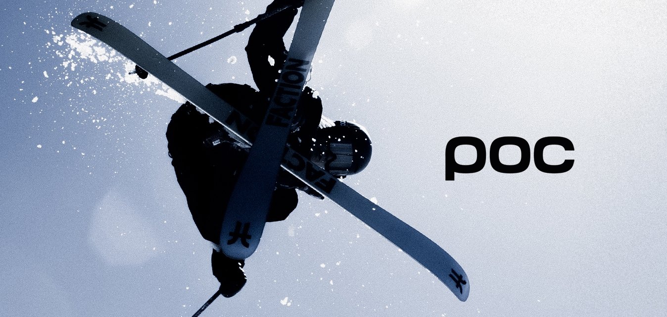 Lyžař předvádějící trik ve vzduchu, oblečený v černém oblečení, na bílých lyžích s logem 