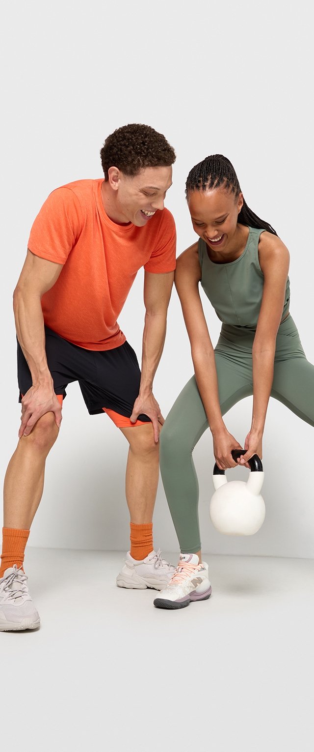 Zwei Personen, die sich fit halten: eine in einem orangefarbenen Shirt und schwarzen Shorts, die andere in einem grünen Trainingsoutfit, die eine weiße Kettlebell hält.