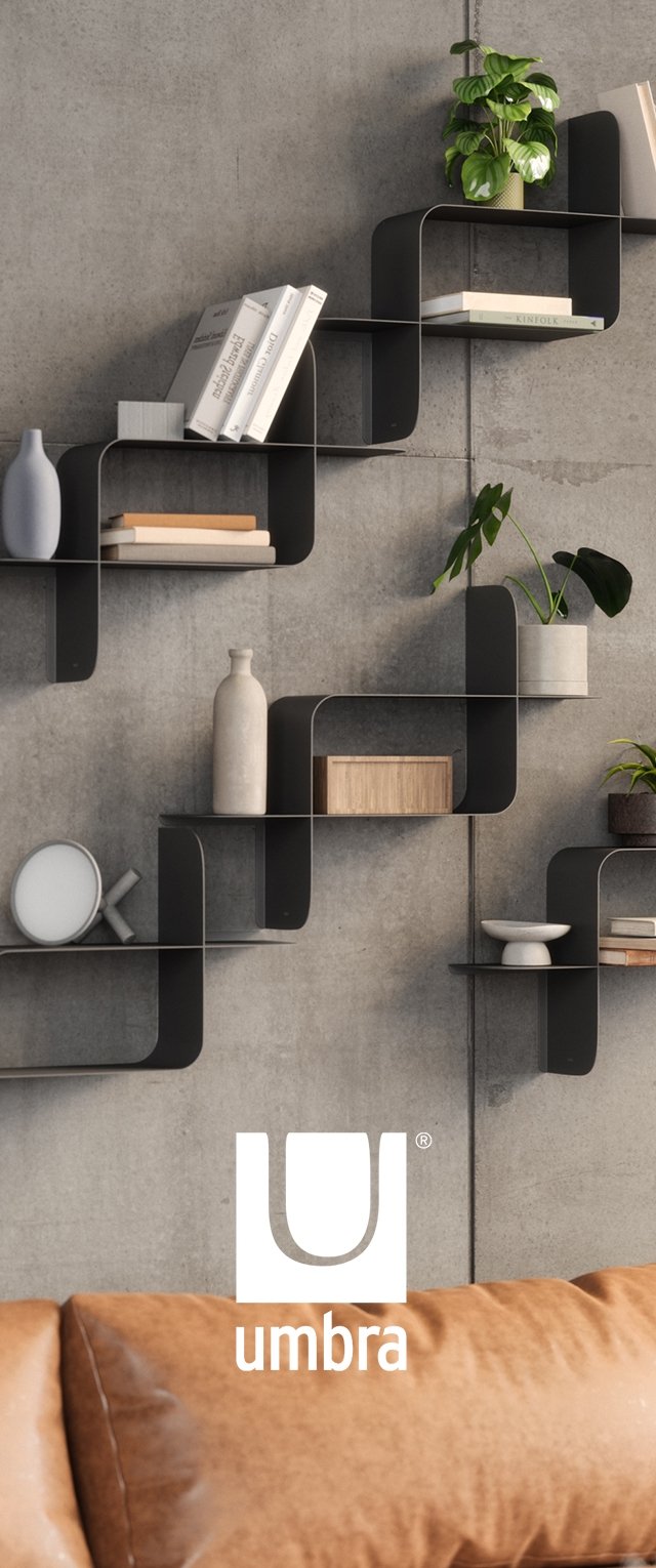 Estantería en zigzag de metal negro montada en una pared de hormigón, que exhibe libros, una planta y objetos decorativos de formas y texturas variadas.