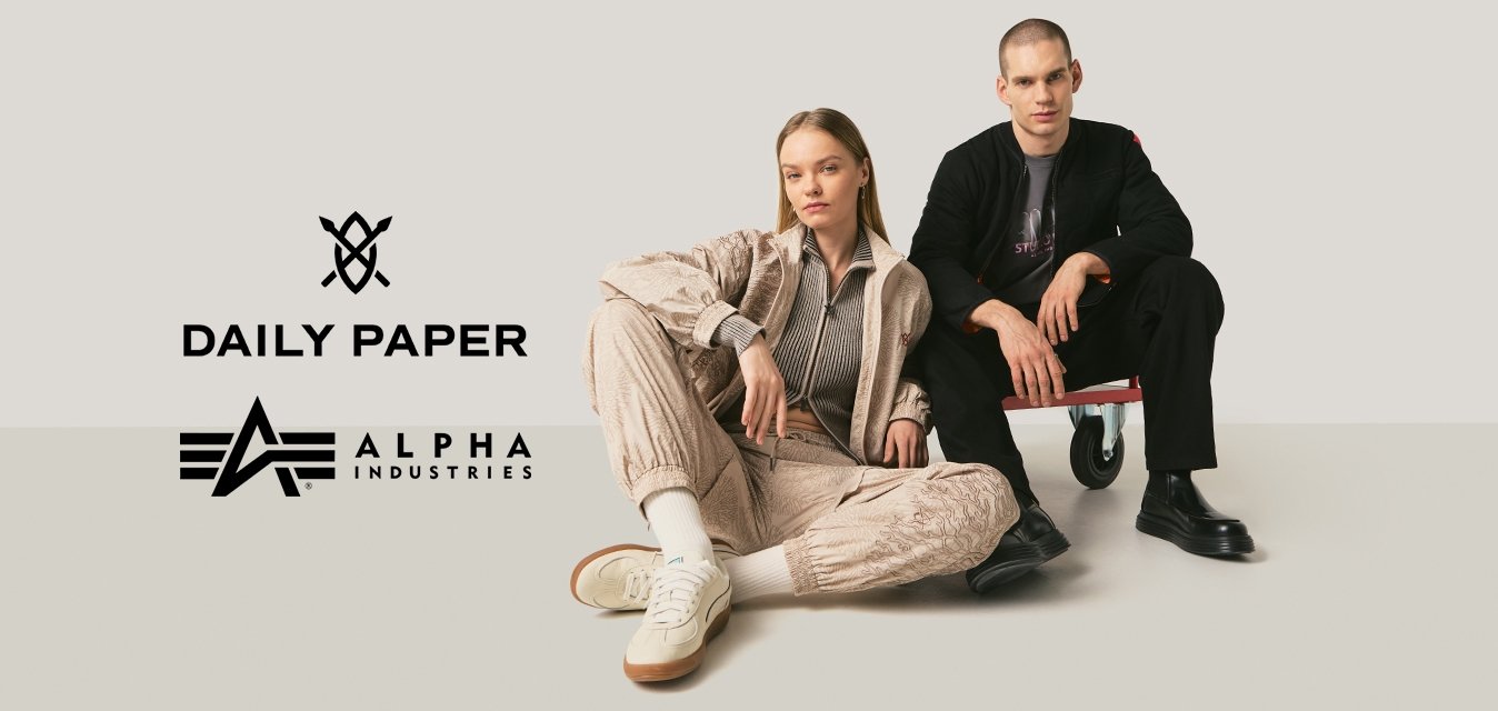 Mladý muž a žena pózují v ležérním streetwearu na jednobarevném pozadí, žena sedí na zemi, muž na malé kolečkové plošině.