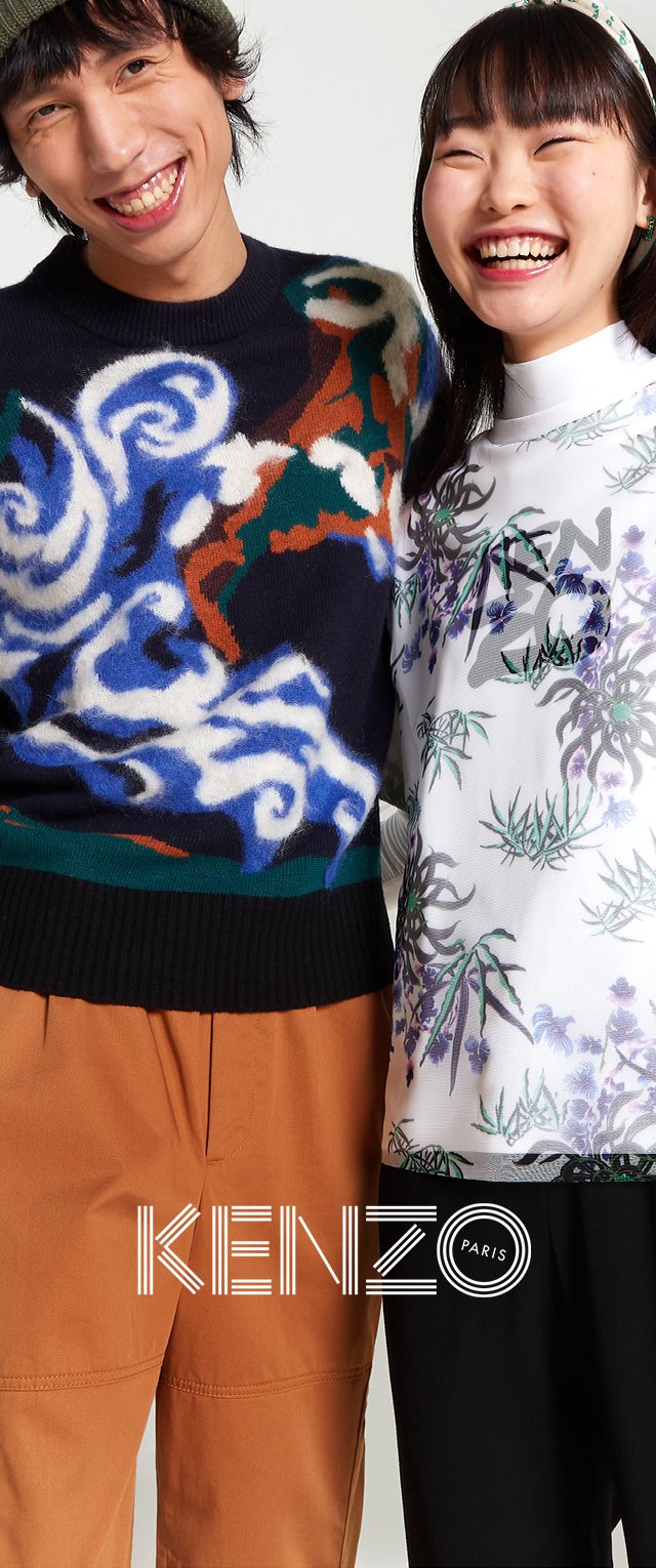Sweter dzianinowy w granatowej bazie z kolorowymi wzorami fal; modelka ma na sobie białą bluzkę w kwiaty. Beżowe spodnie z kieszeniami dopełniają stylizację.