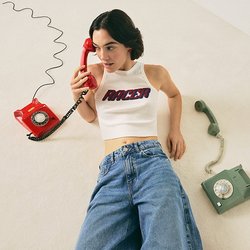 Žena v bílém crop topu a džínách leží na podlaze, drží červený otočný telefon, vedle ní leží zelený otočný telefon.