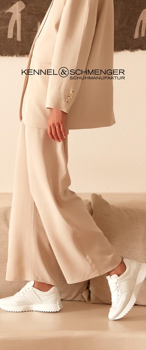 Zapatillas blancas con suelas texturizadas, usadas con pantalones de tela beige sueltos, con una silueta ajustada y detalles sutiles de botones.