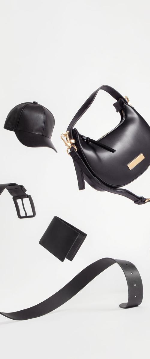 Zwarte leren handtas met gouden hardware, een passende zwarte pet, een slanke riem en een portemonnee, allemaal op een witte achtergrond. Soepele texturen en minimalistischer ontwerp.