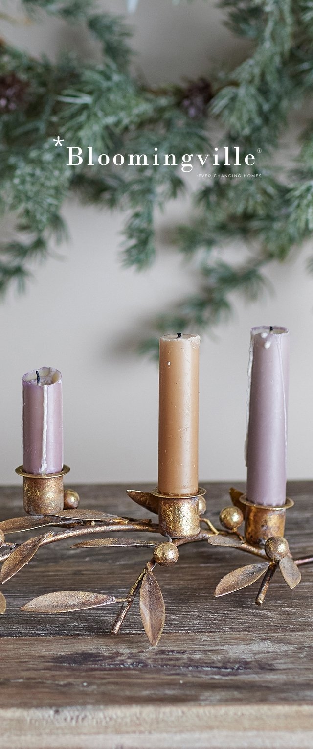 Tres candelabros de metal dorado con acentos de hojas. Las velas son de color púrpura y marrón, variando en altura, colocadas sobre una superficie de madera.