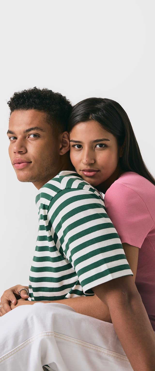 Två individer poserar tillsammans. Den ena har på sig en grön och vit randig skjorta; den andra har en rosa åtsittande topp. Båda har mörkt hår.