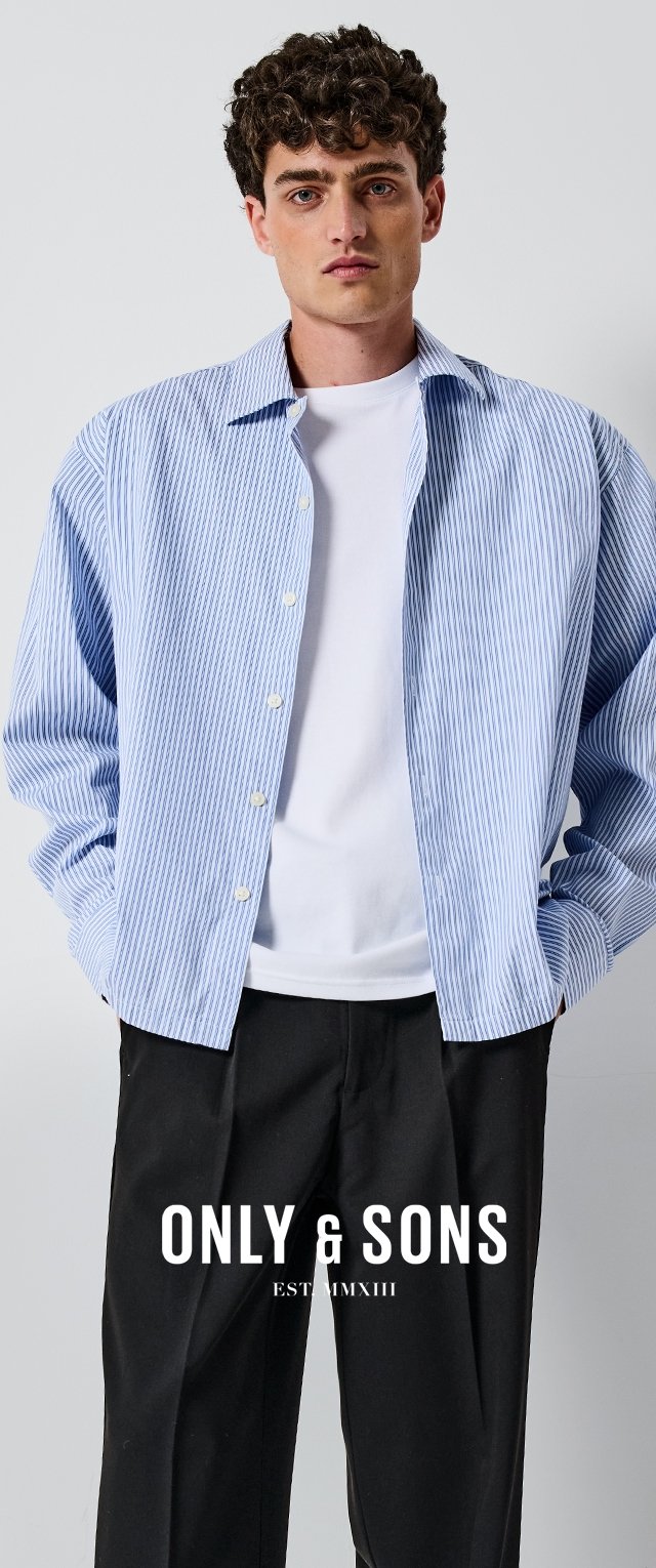 Camisa de rayas azul claro y blanca con botones, de manga larga y ajuste relajado, combinada con una camiseta blanca lisa debajo, usada con pantalones oscuros.