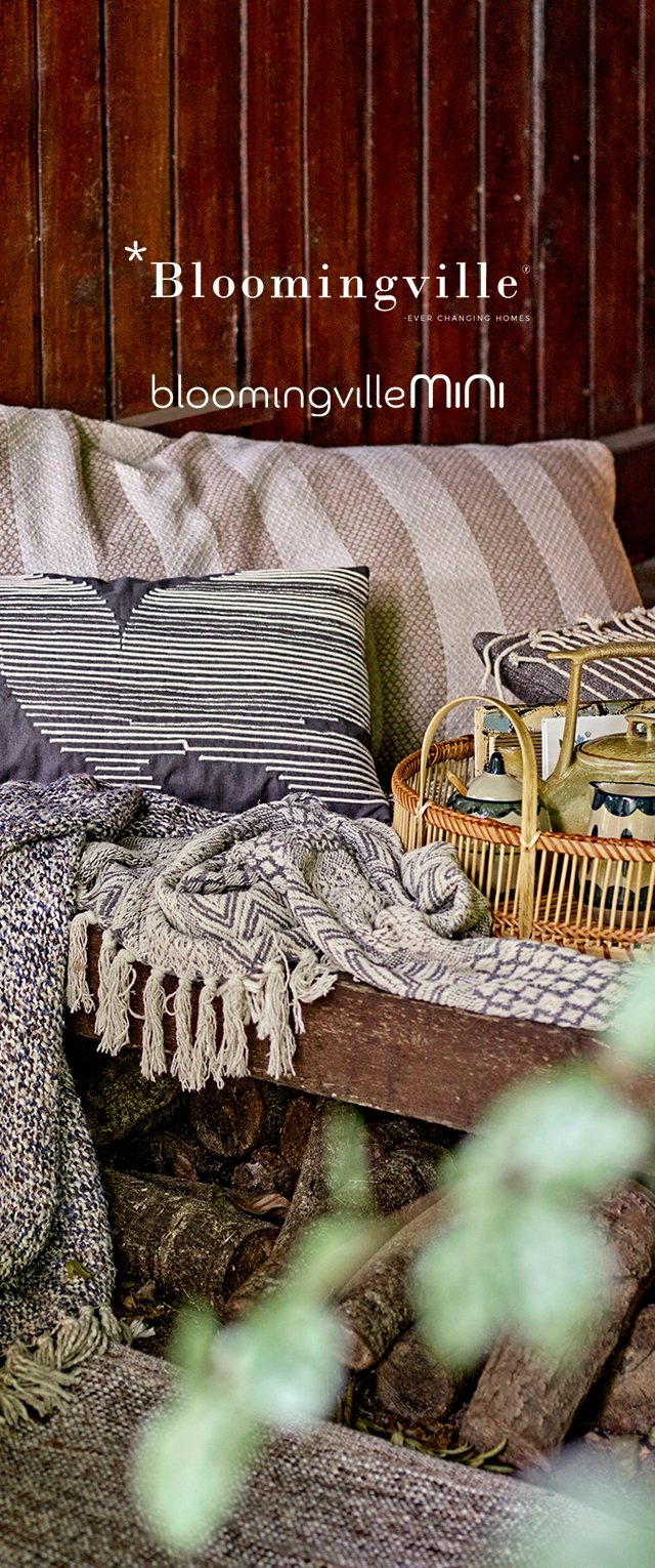 Koselig sitteområde med mønstrede puter, vevde tepper og et kurvbrett med tekanne og kopper mot en trevegg.