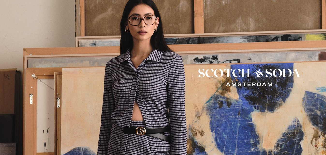 Žena v přiléhavých šatech s kostkovaným vzorem v námořnické modři a bílé, s knoflíky a tříčtvrtečními rukávy, doplněná černým pásem a sandály.