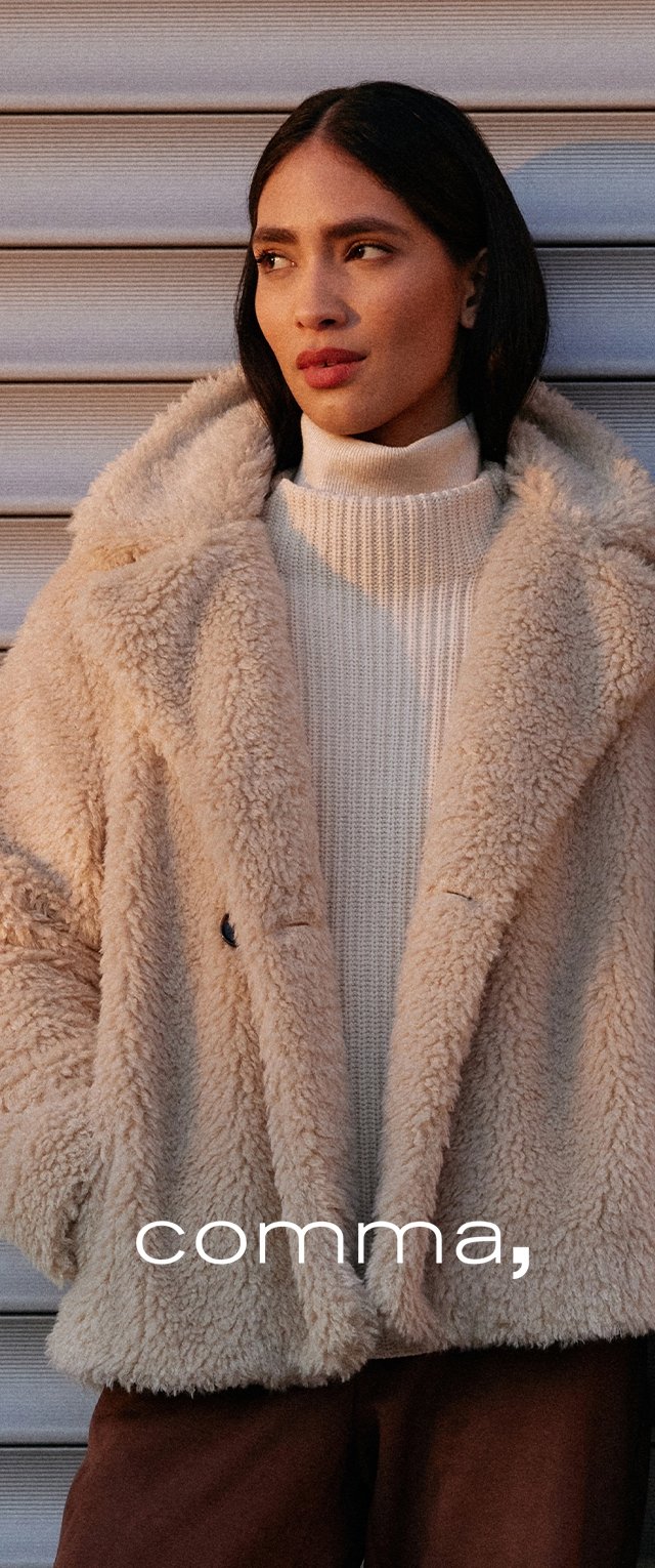 Beige nepbontjas met een zachte textuur, dubbelgeknoopte sluiting en grote kraag, gedragen over een crème ribgebreide coltrui.