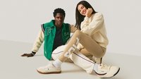 Grüne Collegejacke mit schwarzen und weißen Akzenten, beiger Sweatshirt, beigen Leggings mit weißem Logo und cremefarbenen Sneakers mit dunkler Sohle.