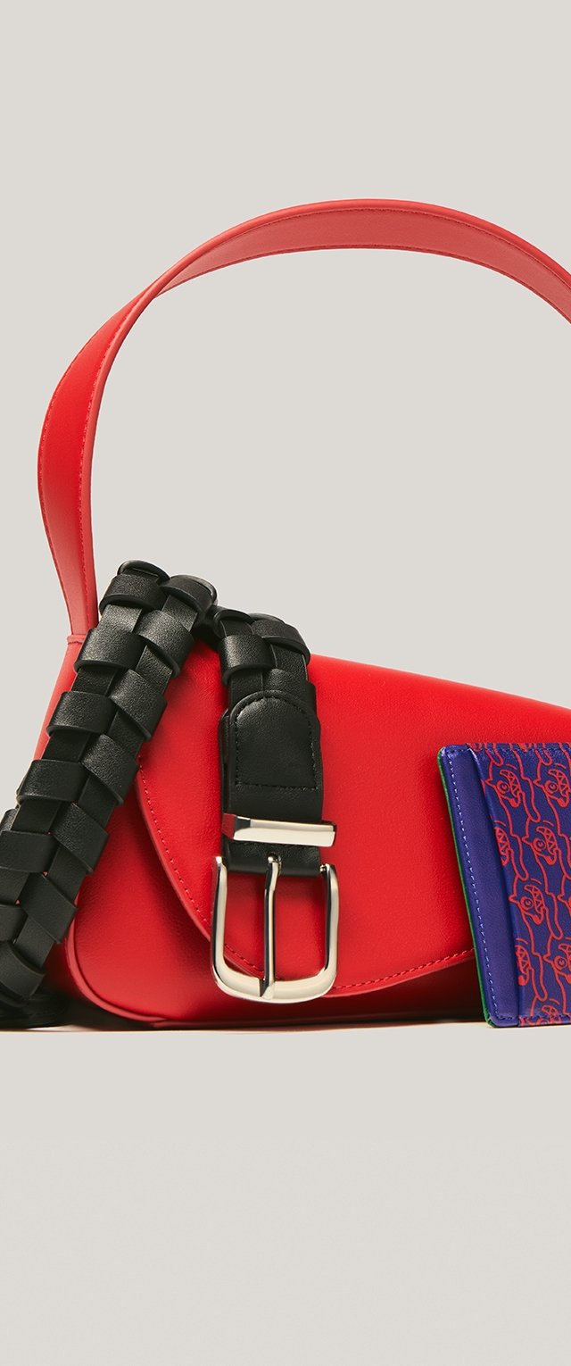 Rote strukturierte Handtasche mit glatter Oberfläche, ausgestattet mit einem schwarzen geflochtenen Träger und einem blauen Kartenetui mit rotem Muster. Silberne Schnallendetail.