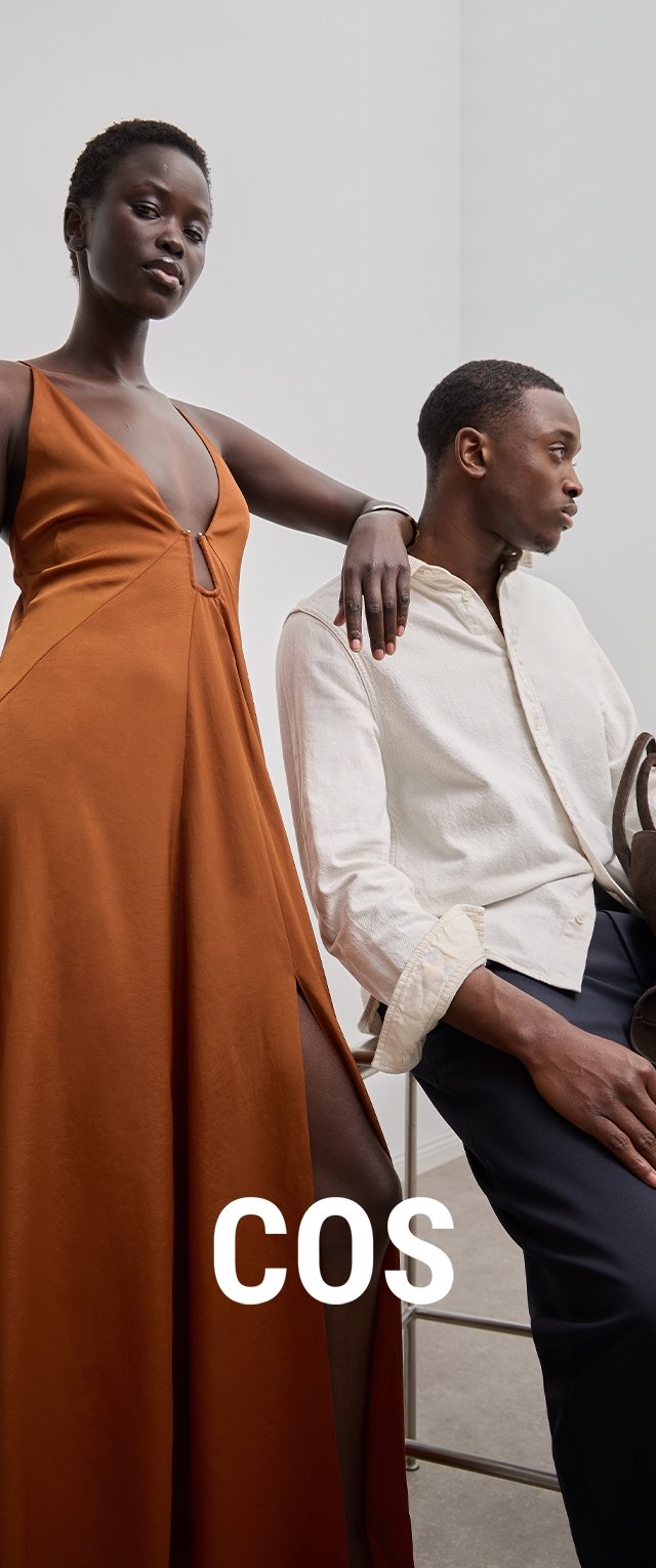 Vestido largo de color óxido con un profundo escote en V y abertura lateral. La modelo lleva una camisa abotonada de textura color crema y pantalones azul marino.