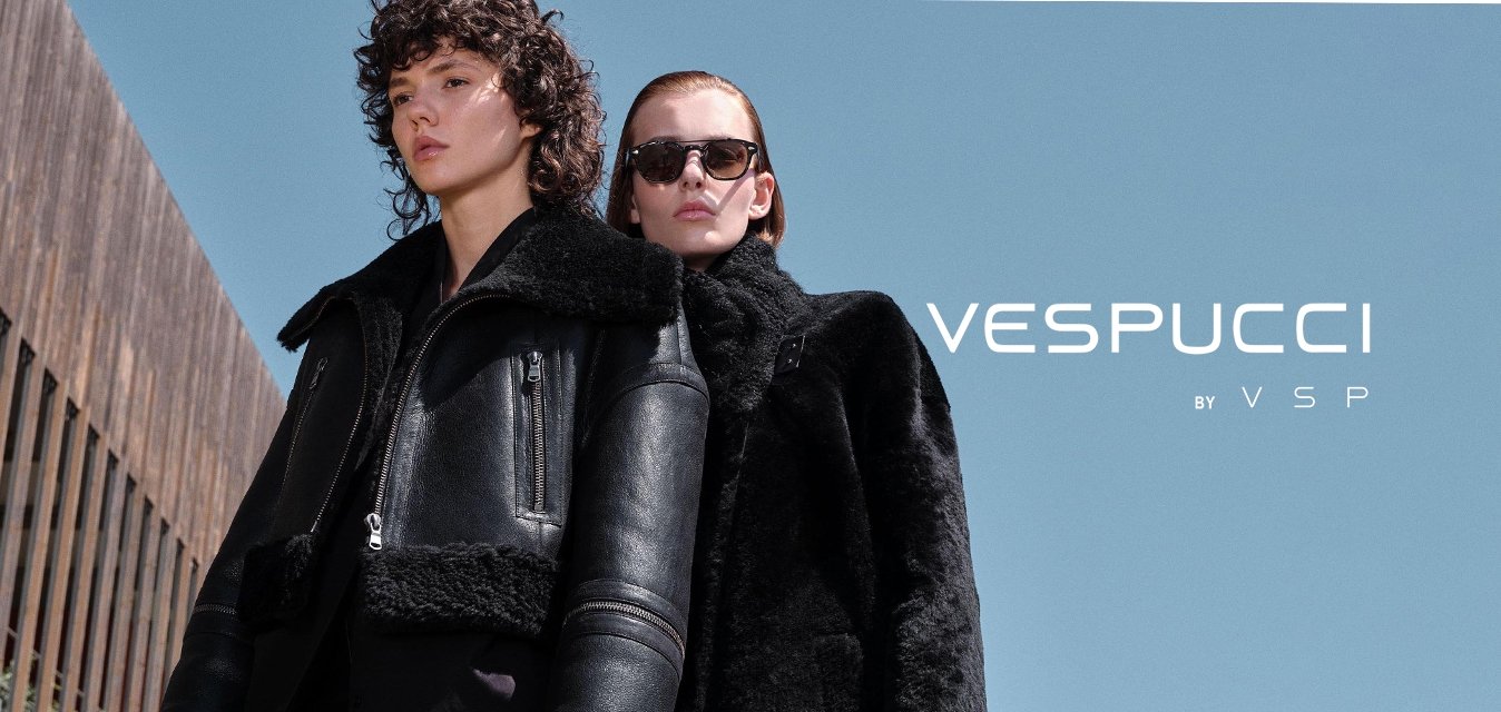 Dvě ženy mají na sobě černé svrchní oblečení: jedna v kožené bundě s ovčím rounem a zipy; druhá v texturovaném černém kabátu. Nad nimi je jasně modrá obloha.