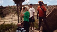 Gruppe von vier Personen im Freien in der Nähe von Felsformationen. Eine Frau in einem grünen Shirt benutzt ein Fernglas. Die anderen tragen legere Kleidung und Hüte.