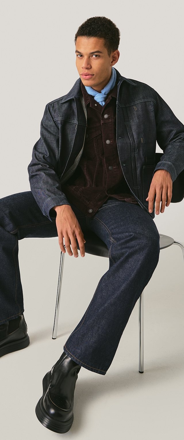 Chaqueta vaquera con un acabado azul oscuro, sobre una camisa de pana burdeos. Pantalones estilo militar en denim oscuro. Botas negras robustas.