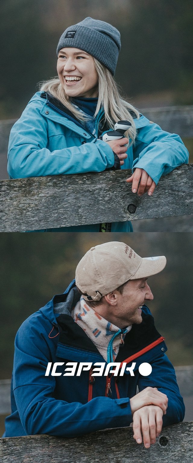 Blaue Jacke mit roten Akzenten, graue Mütze und hellgraßer Schal, beide Personen lächeln, stehen an einem Holzgeländer in einer Außenumgebung.