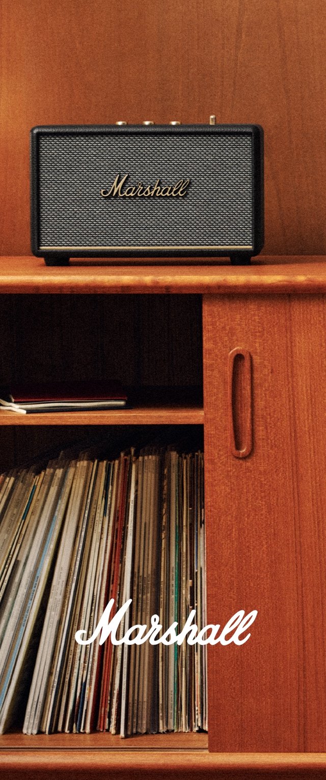 Marshall-Lautsprecher in Schwarz mit strukturierter Vorderseite, goldenem Logo und Bedienknöpfen, auf einem Holzregal über gestapelten Schallplatten platziert.