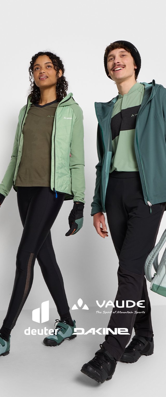 Due individui indossano abbigliamento da esterno. La donna ha una giacca trapuntata verde chiaro e leggings scuri, mentre l'uomo indossa un hoodie teal e pantaloni neri.
