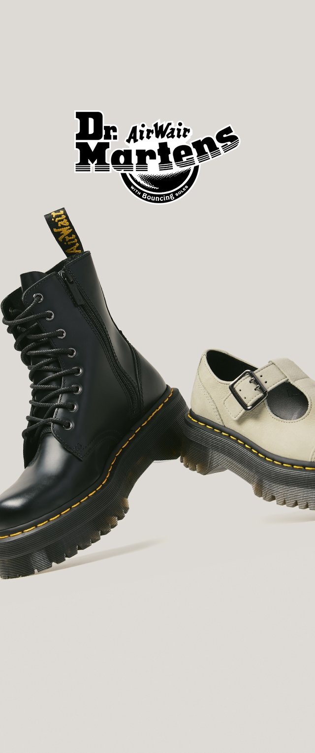 Zwarte leren veterlaars en beige Mary Jane schoen met geel gestikte dikke zolen, naast elkaar geplaatst, Dr. Martens-logo erboven.