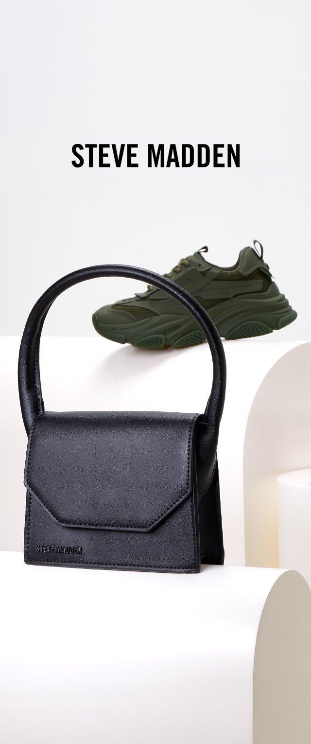 Zwarte faux leren handtas met een gebogen handvat en een klep aan de voorkant. Heeft een gegraveerde merknaam. Groene chunky sneakers op de achtergrond.