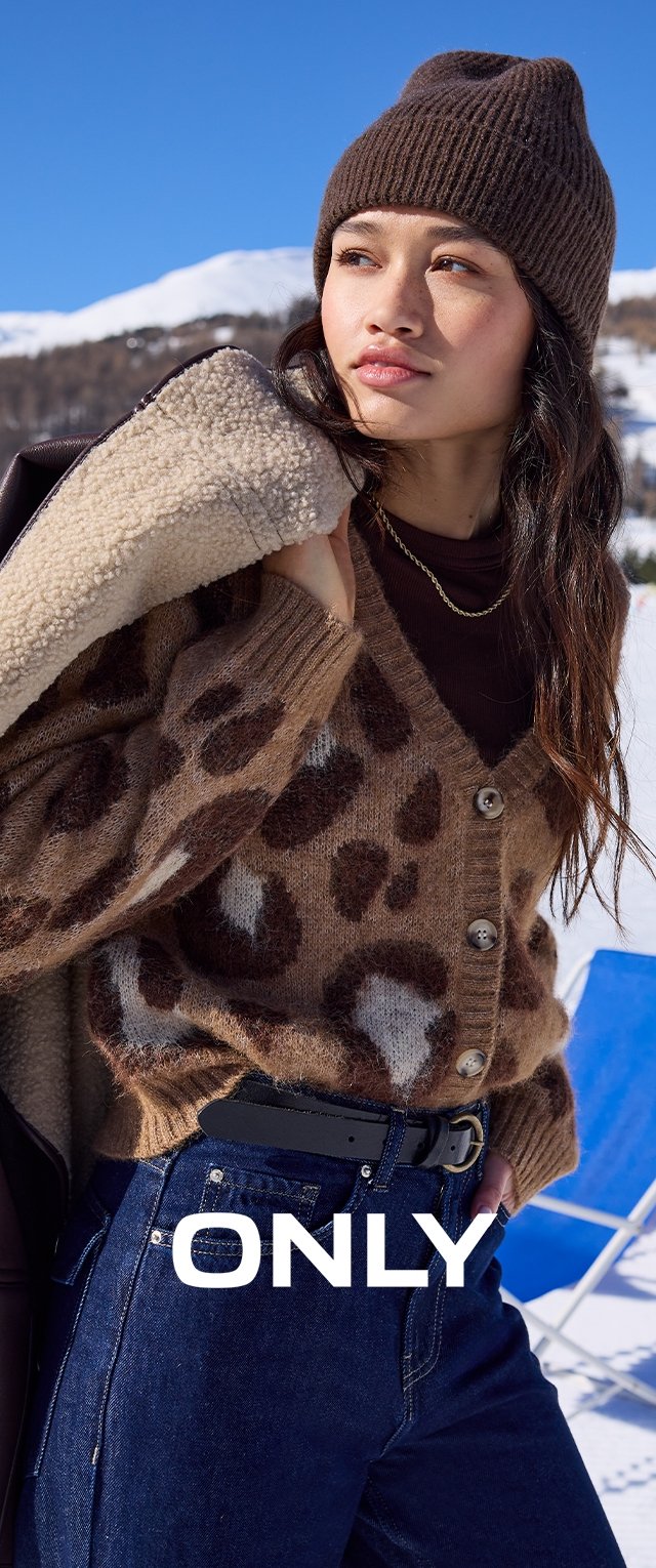 Cárdigan marrón con estampado de leopardo y botones, llevado sobre una camiseta oscura; combinado con jeans de mezclilla oscuros y un gorro acanalado marrón. Escenario al aire libre.