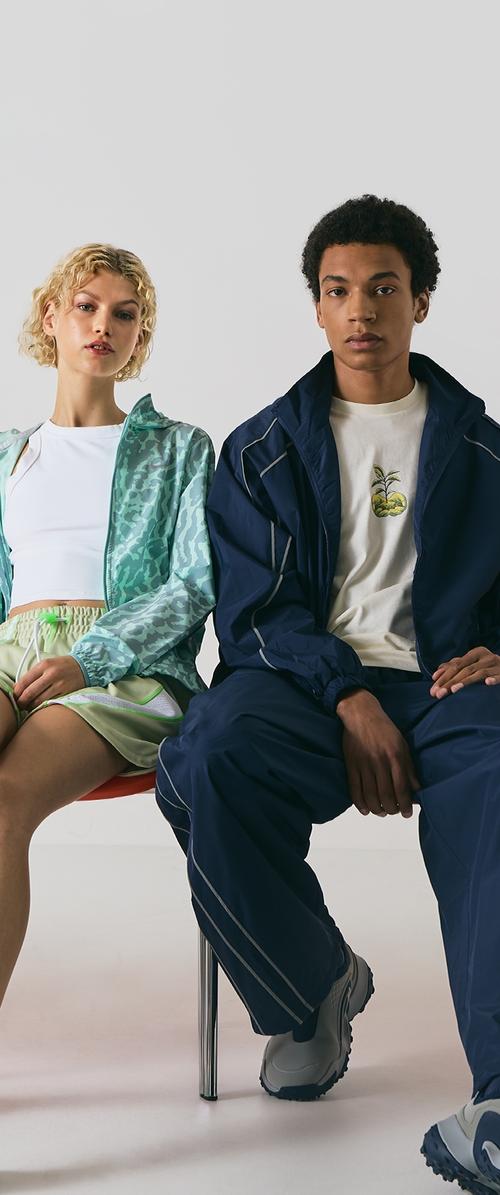 Giacca leggera e trasparente di colore menta con motivo astratto, abbinata a un top bianco e a pantaloni corti verdi. Tuta in blu scuro con grafica di piante.