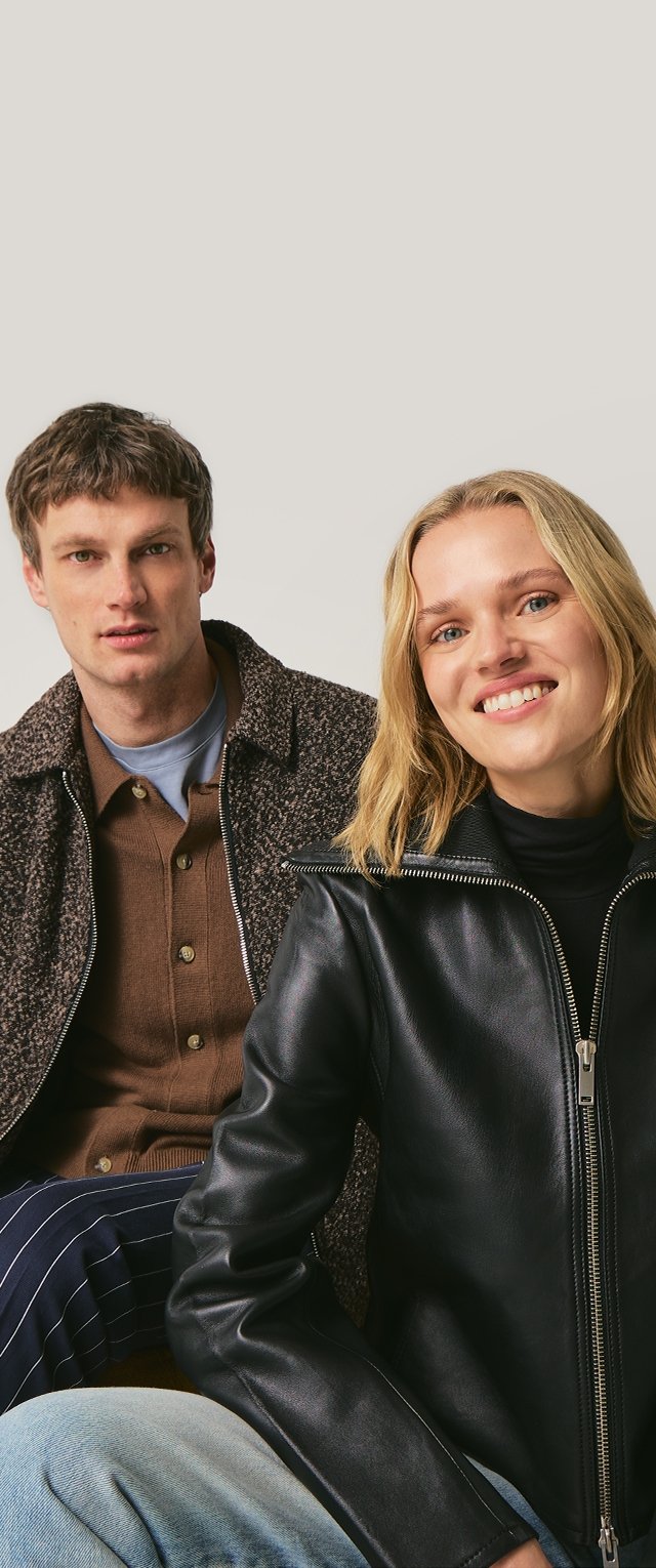 Schwarze Lederjacke mit Reißverschluss, getragen von einem Modell. Grauer Pullover, getragen von einem anderen Modell. Gestreifte Hose sichtbar. Neutraler Hintergrund.