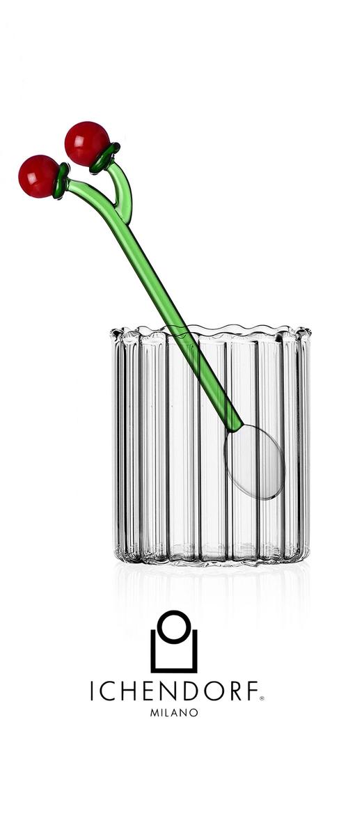 Durchsichtiger Glasbecher mit vertikaler Rippstruktur, ausgestattet mit einem grünen Glasrührstab, der oben mit zwei kirschartigen roten Kugeln versehen ist.