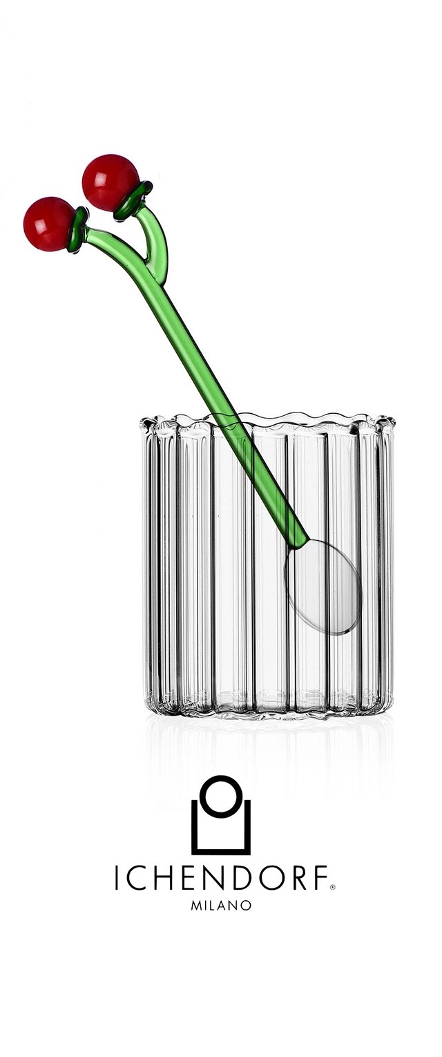Tasse en verre transparent avec une texture à rainures verticales, dotée d'une agitateur en verre vert surmonté de deux sphères rouges ressemblant à des cerises.