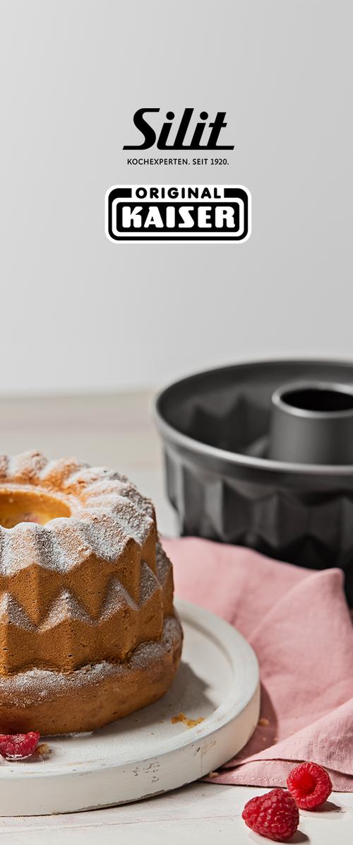 Bundt pyragas pabarstytas cukraus pudra ant balto lėkštės, juoda kepimo forma ir rožinis audinys fone, šalia šviežios avietės.