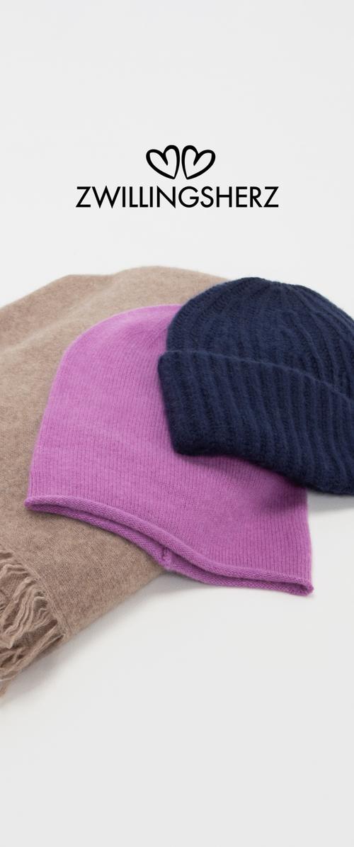 Collezione di tre cappelli lavorati a maglia: un cappello rigato di un blu navy scuro, un berretto viola morbido e una sciarpa marrone con frange, disposti in piano su uno sfondo bianco.