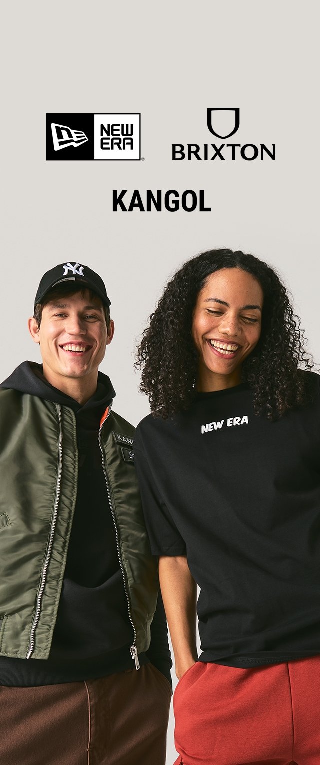 Dos personas visten ropa casual: una con una chaqueta bomber verde y una sudadera con capucha negra, la otra con una camiseta negra y pantalones rojos.