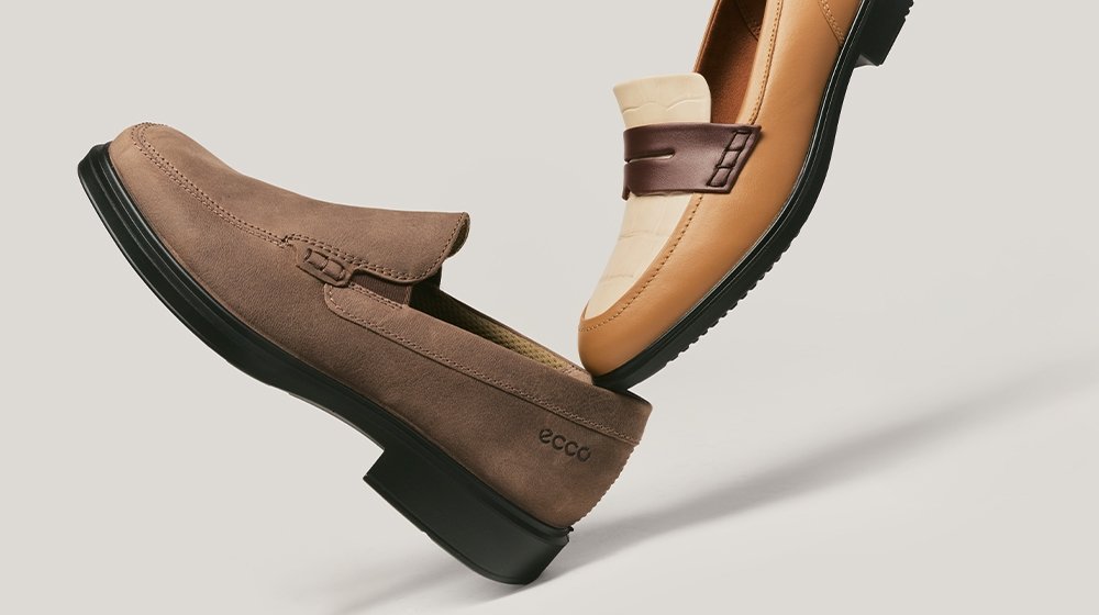 Zwei Leder-Loafer für Herren, ein hellbraunes mit dunklem Riemen und eines aus braunem Wildleder mit schwarzer Sohle, auf einem neutralen hellen Hintergrund präsentiert.