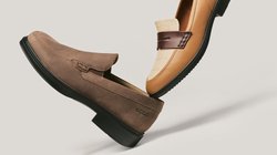 Zwei Leder-Loafer für Herren, ein hellbraunes mit dunklem Riemen und eines aus braunem Wildleder mit schwarzer Sohle, auf einem neutralen hellen Hintergrund präsentiert.