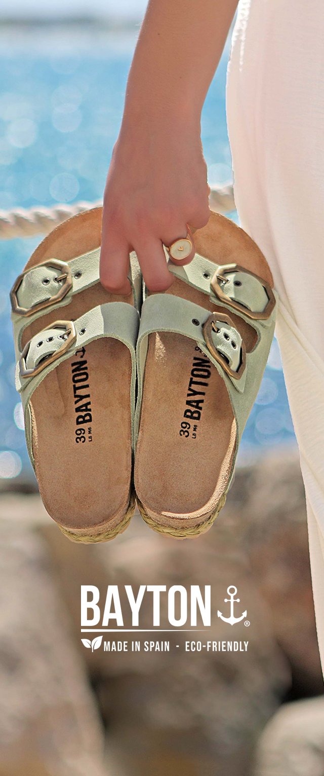 Sandali in suede verde con due cinturini regolabili e fibbie in metallo. Fodera in sughero con una suola beige texturizzata. Nome del marchio "BAYTON" visibile.