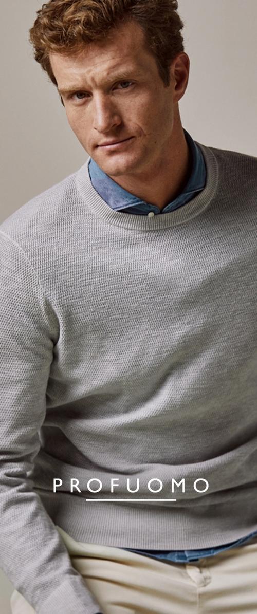 Jersey de punto gris claro con acabado texturizado, cuello redondo, llevado sobre una camisa azul chambray, combinado con pantalones de color claro.