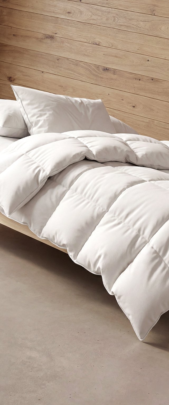 Trapunta bianca e cuscini su un letto con parete in pannelli di legno chiaro e pavimento beige in un ambiente minimalista.