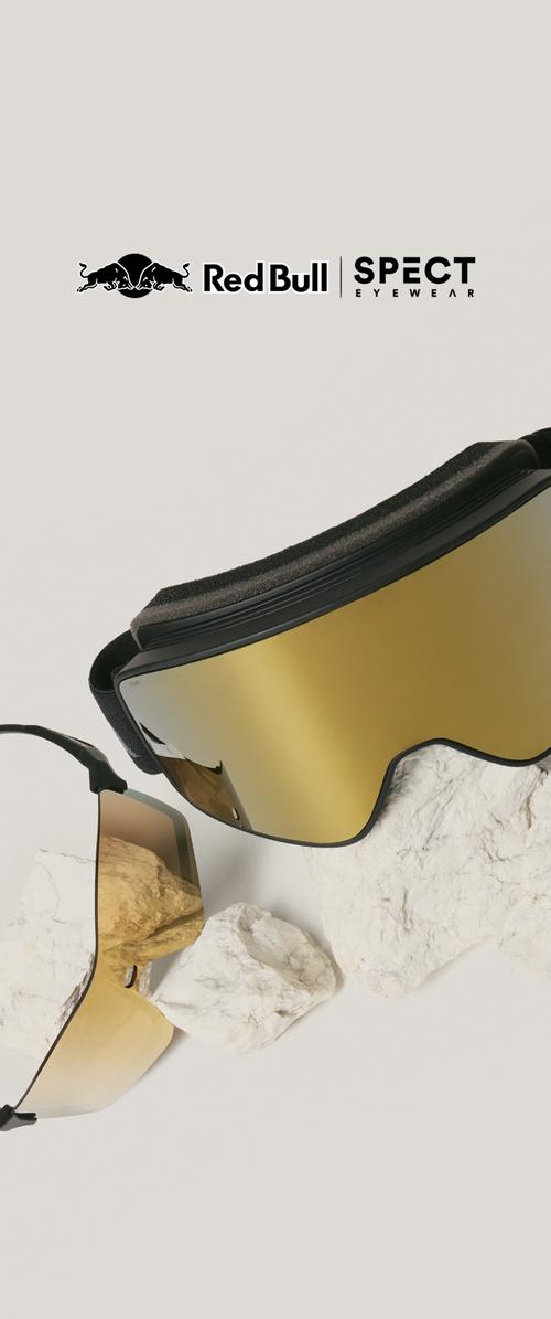 Lunettes de ski et lunettes de soleil à teinte dorée avec des montures noires reposent sur des rochers blancs, logo Red Bull SPECT Eyewear au-dessus sur un fond clair.