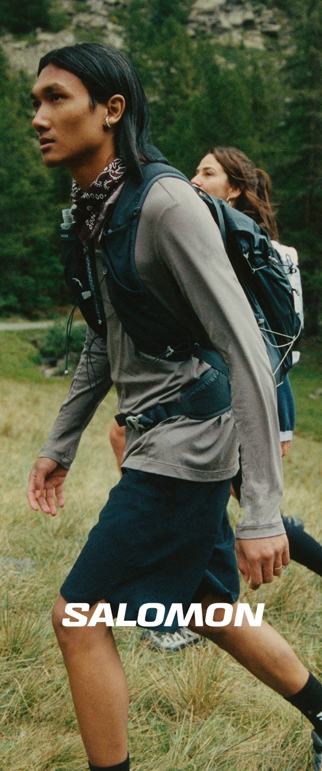 Salomon-Markenoutdoor-Ausrüstung; männliches Model in grauem Langarmshirt und schwarzen Shorts; mit einem strukturierten Rucksack; natürliche Umgebung.