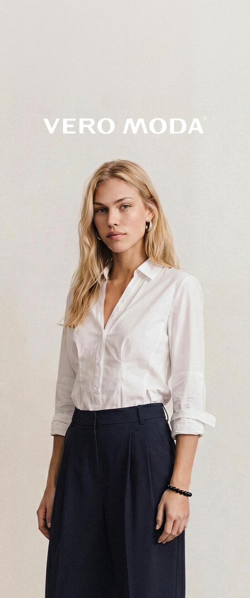 Femeie blondă purtând o cămașă albă cu nasturi și pantaloni negri cu talie înaltă stă pe un fundal simplu și luminos, cu sigla Vero Moda deasupra.