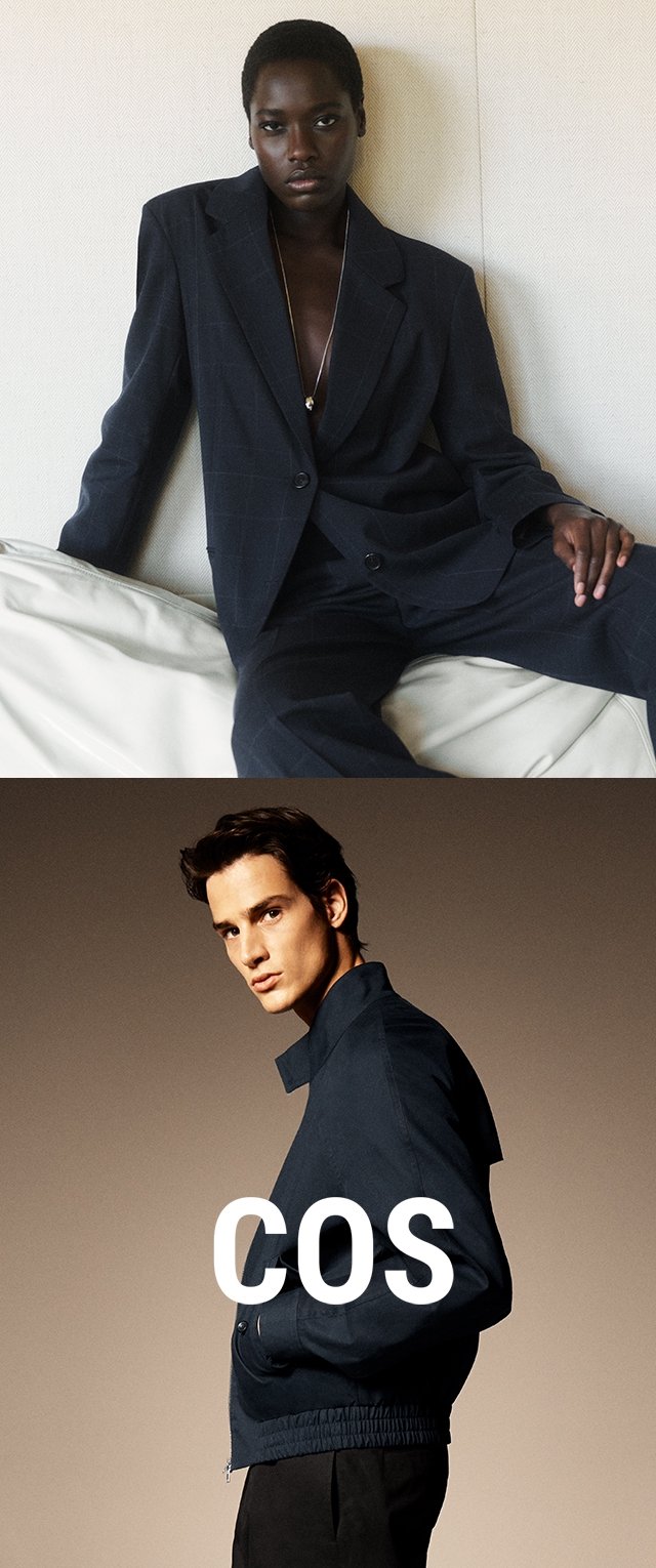 Schwarze Frau in dunklem, übergroßem Anzug sitzt vor weißer Wand; weißer Mann in marineblauer Jacke und Hose posiert seitlich mit überlagertem "COS"-Logo.