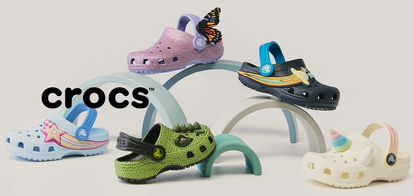 Pět barevných dětských dřeváků s dekorativními přívěsky uspořádaných na pastelových obloucích na neutrálním pozadí.