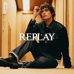 Mladý muž v džínsové bundě a džínách sedí na kobercové podlaze úzké béžové chodby a jednou rukou si dotýká vlasů.