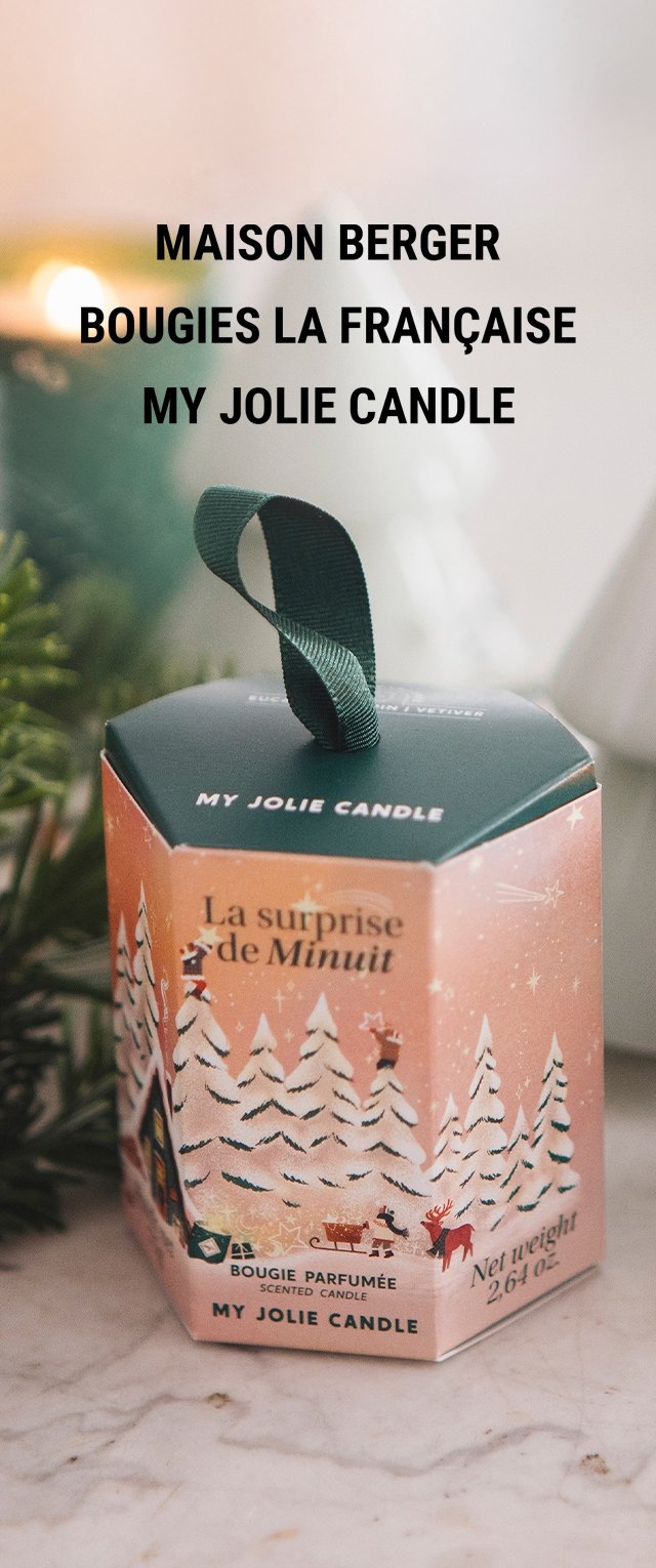 Embalaje de cartón hexagonal en rosa suave con ilustraciones de escenas invernales, acentos verdes y un asa de cinta a juego. Contiene una vela aromática.